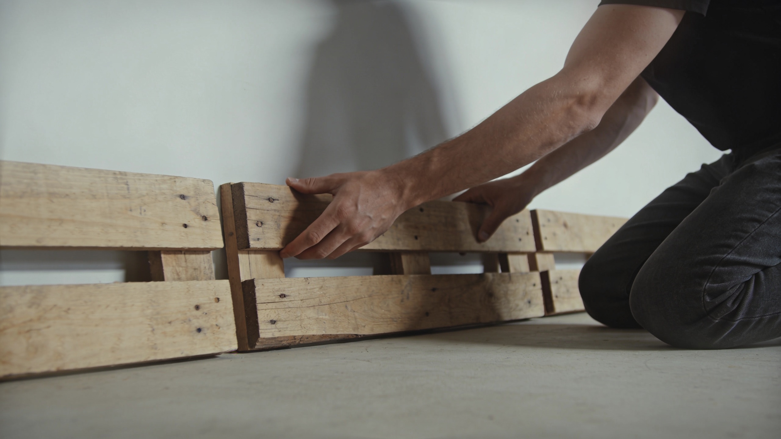 Homme agenouille posant des palettes bois contre mur
