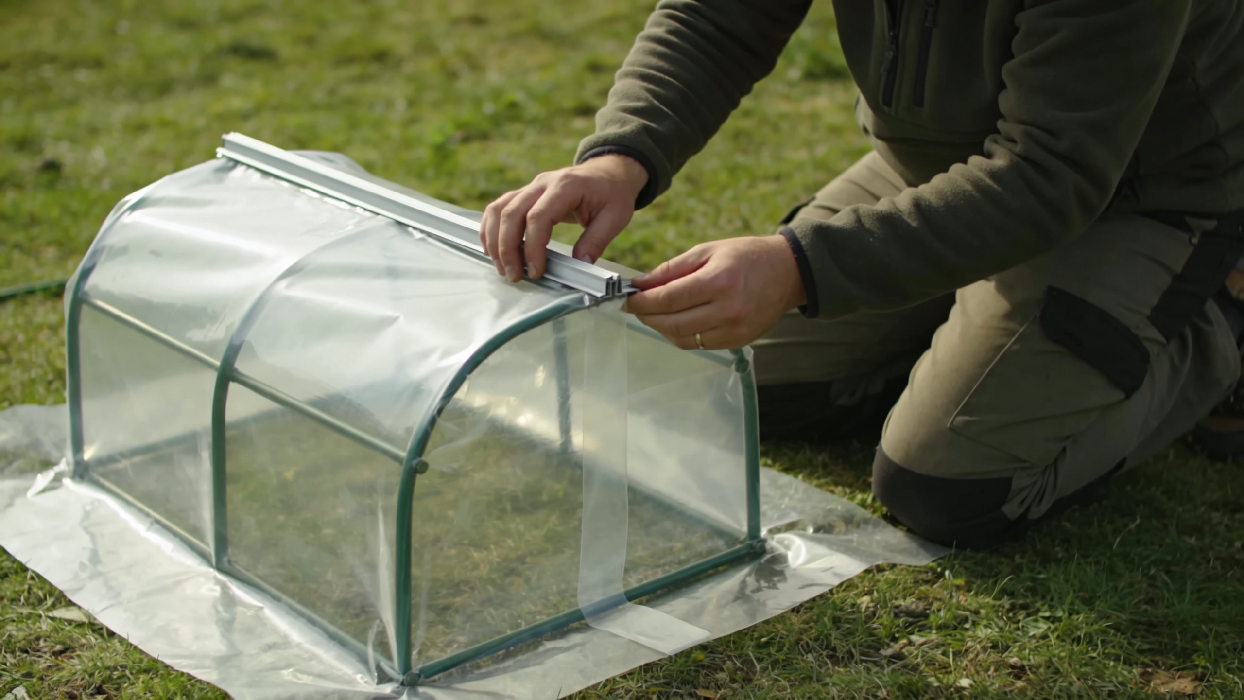 homme agenouille construisant petite serre jardin plastique transparent