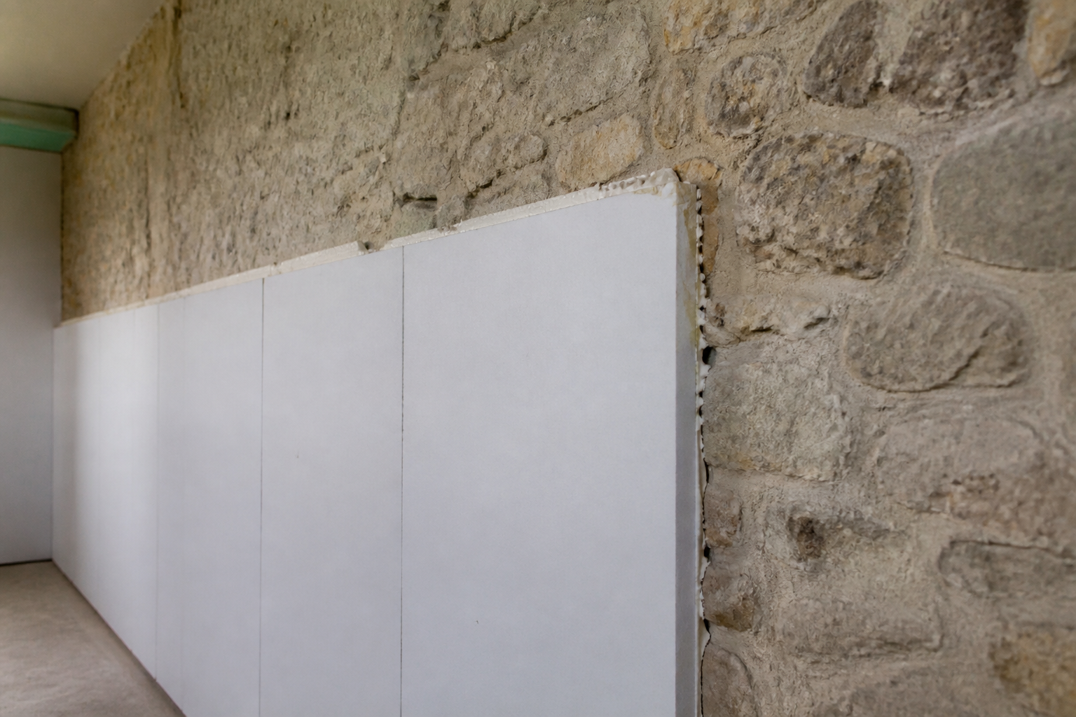 Panneaux isolants blancs colles sur mur pierre brute interieur