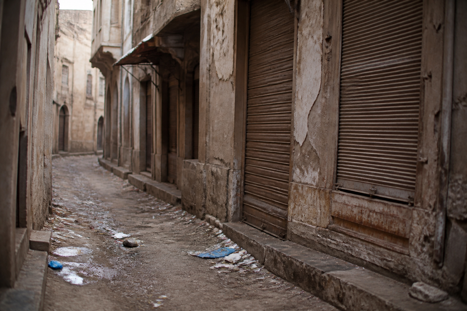 Rue etroite avec immeubles degrades, detritus au sol, volets fermes