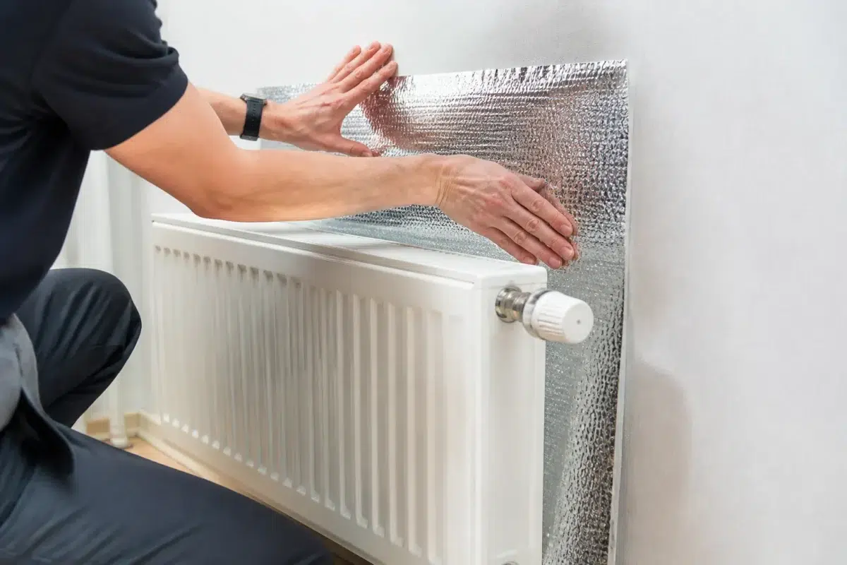 Personne collant film reflecteur argente derriere radiateur blanc