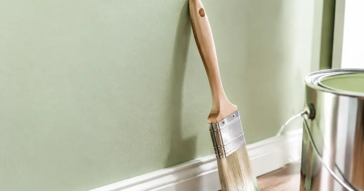 Mur peint en teinte sage clair avec pinceau posé contre la surface