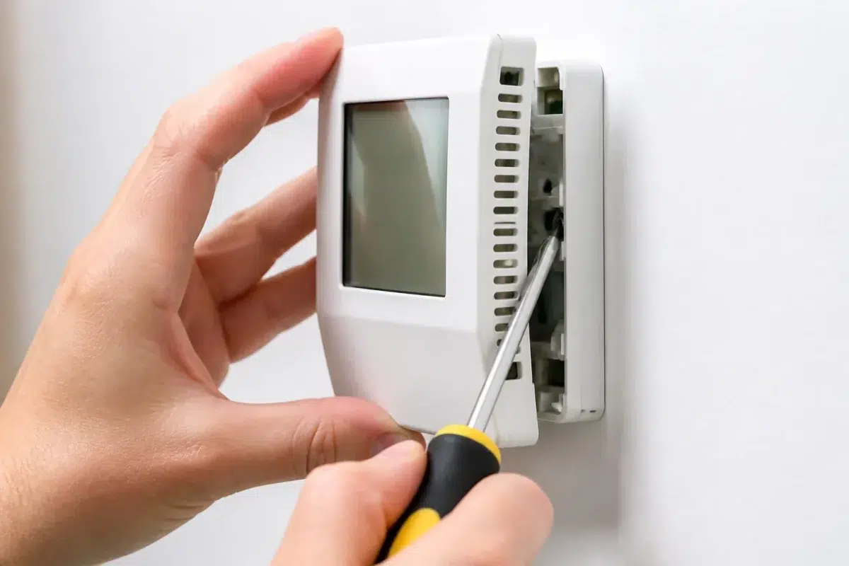 Main ouvrant panneau thermostat avec tournevis cruciforme visible