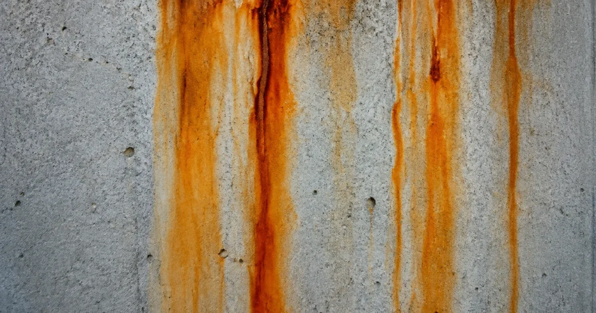 Traces rouille orange coulant verticalement sur beton gris