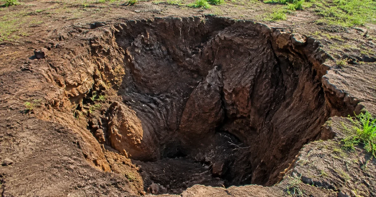 Large gouffre erode dans sol argileux brun fonce