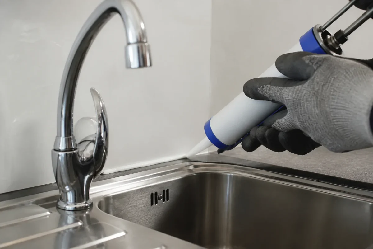 Mains gantees appliquant un joint silicone sur evier